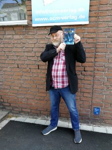 Buchübergabe: Markus Veith mit seinem neuen Buch „Die erste Bahn“ im Freien, vor der Haustür des OCM Verlags. (2021)