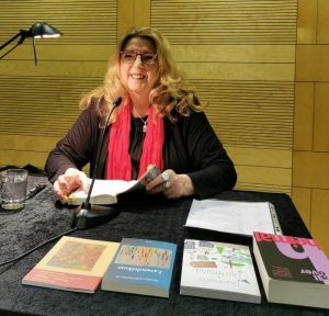 Sigrid Drübbisch sitzt an einem Tisch in der Stadt- und Landesbibliothek Dortmund und hält ihren neuen Krimi Mord-Art in der Hand.