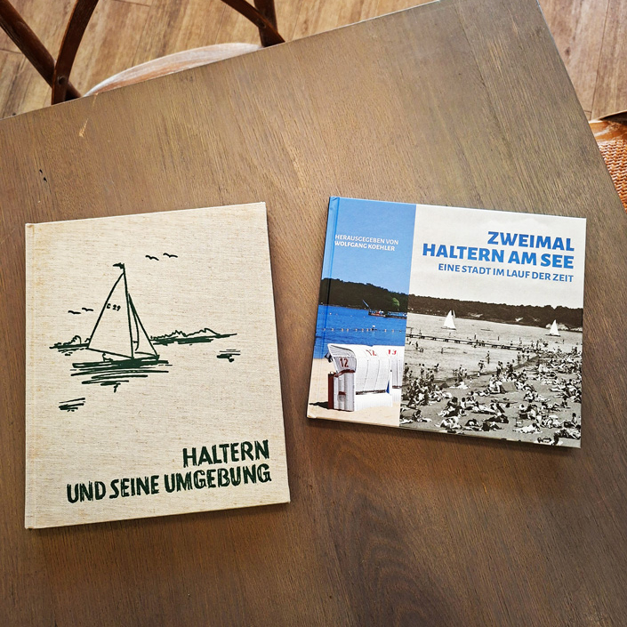 Draufsicht auf zwei Bücher nebeneinander auf einem Holztisch: links das ältere Buch „Haltern und seine Umgebung“ mit einer Segelboot-Illustration, rechts der neue Bildband „Zweimal Haltern am See – Eine Stadt im Lauf der Zeit.