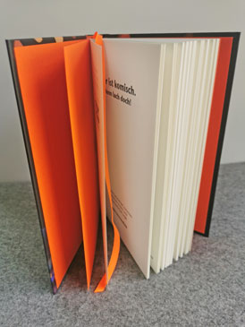 Das offene Buch „Mir ist komisch. Dann lach doch!“ von Leslie Sternenfeld mit orangefarbenem Lesebändchen und Vorsatzpapier.